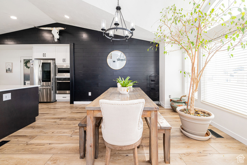 Dining area featuring vaulted ceiling, light wood-style flooring, a chandelier, baseboards, and recessed lighting