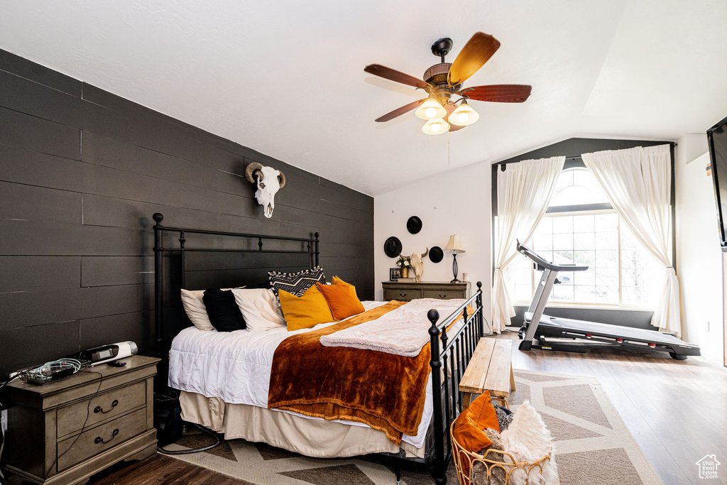 Bedroom featuring vaulted ceiling, dark wood-style floors, a ceiling fan, and wooden walls