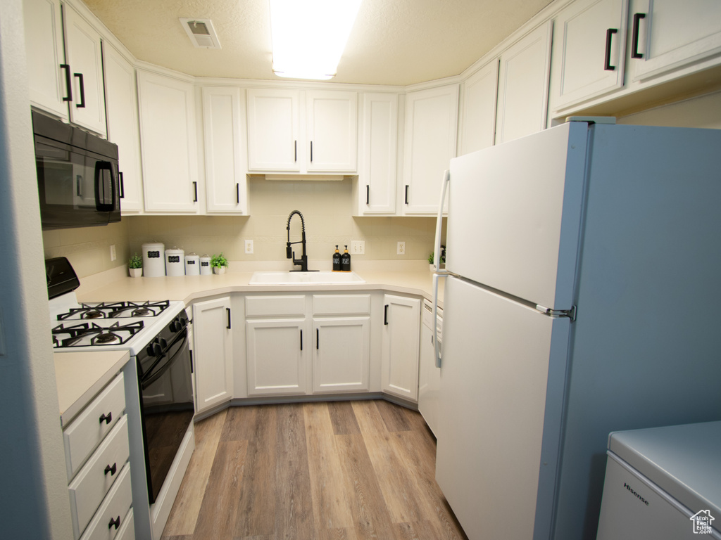Kitchen featuring black microwave, gas range, freestanding refrigerator, a sink, and light wood finished floors