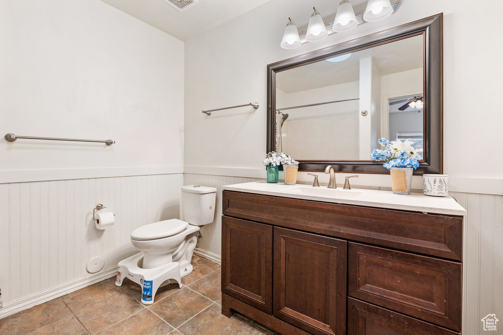 Bathroom with wainscoting, toilet, vanity, tile patterned floors, and a ceiling fan