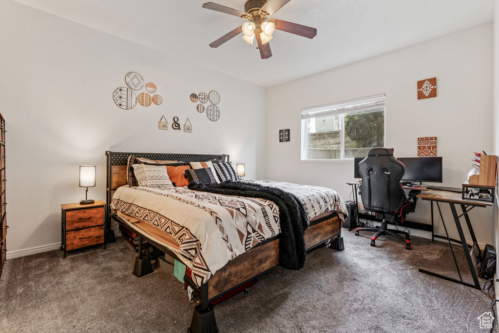 Carpeted bedroom featuring an office area, ceiling fan, and baseboards