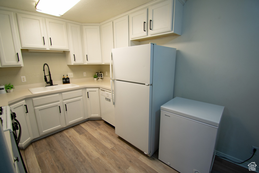 Kitchen featuring white appliances, a sink, white cabinetry, light wood-style floors, and light countertops