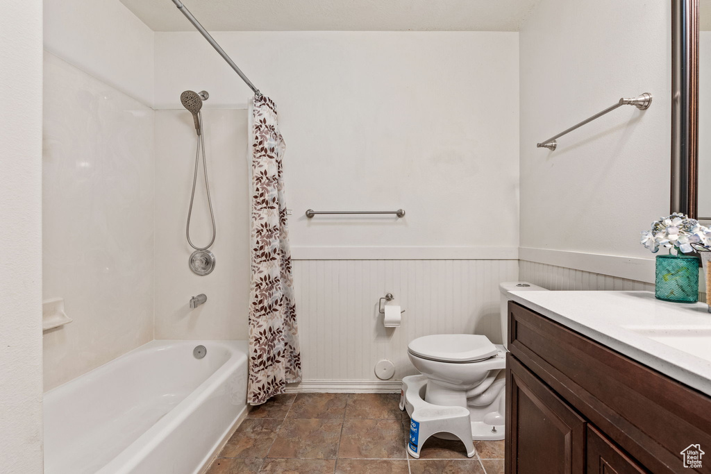 Bathroom with toilet, wainscoting, vanity, baseboards, and shower / bath combo with shower curtain
