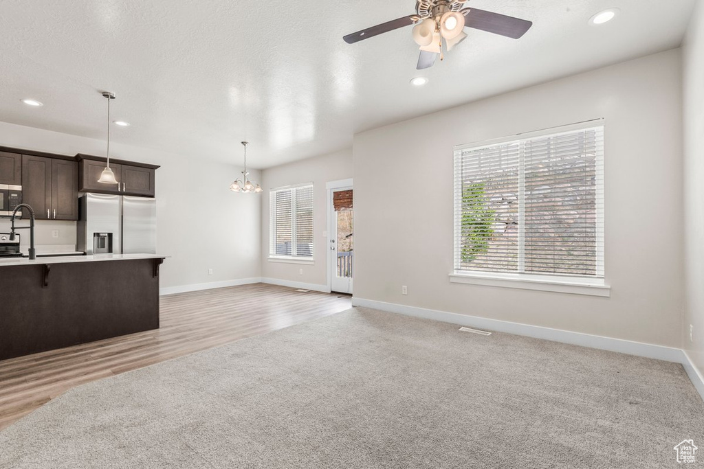 Unfurnished living room featuring a chandelier, a ceiling fan, recessed lighting, baseboards, and light colored carpet