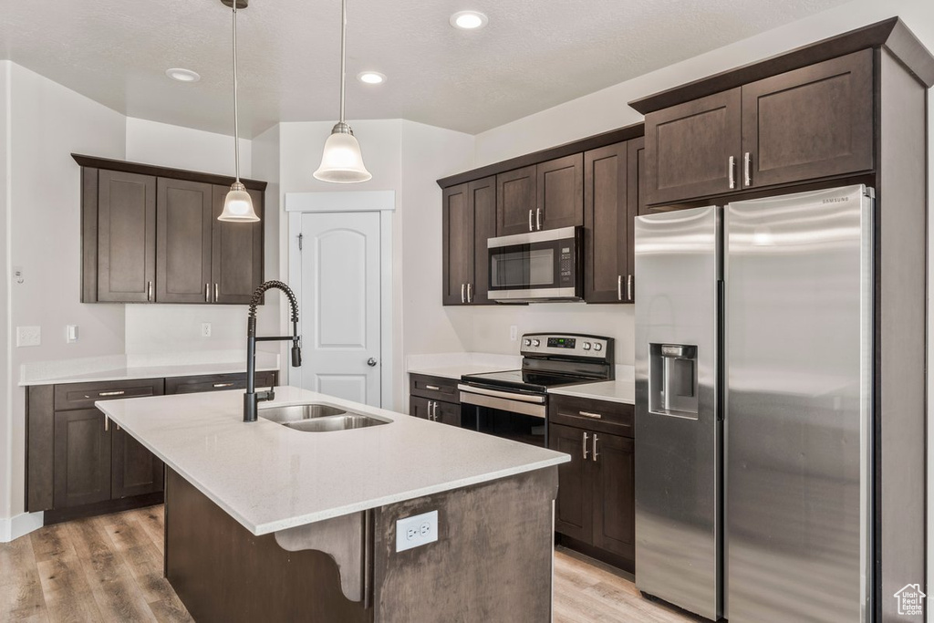 Kitchen featuring stainless steel appliances, a sink, dark brown cabinetry, a center island with sink, and light wood-style floors