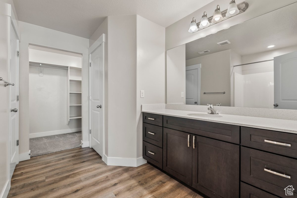 Full bath with wood finished floors, baseboards, vanity, a spacious closet, and a shower