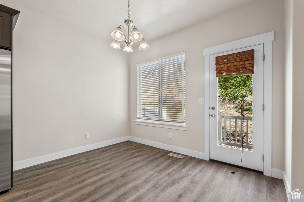 Unfurnished dining area featuring a chandelier, plenty of natural light, and wood finished floors