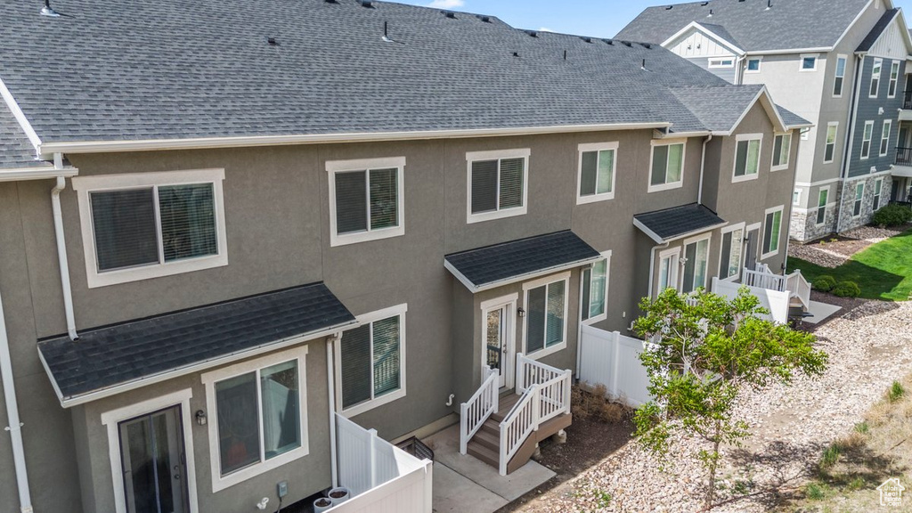 Back of property featuring stucco siding, fence, and a shingled roof