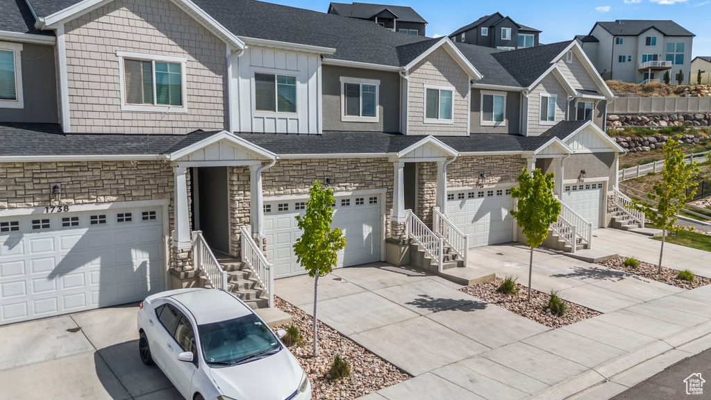 Townhome / multi-family property with board and batten siding, stone siding, concrete driveway, a shingled roof, and an attached garage