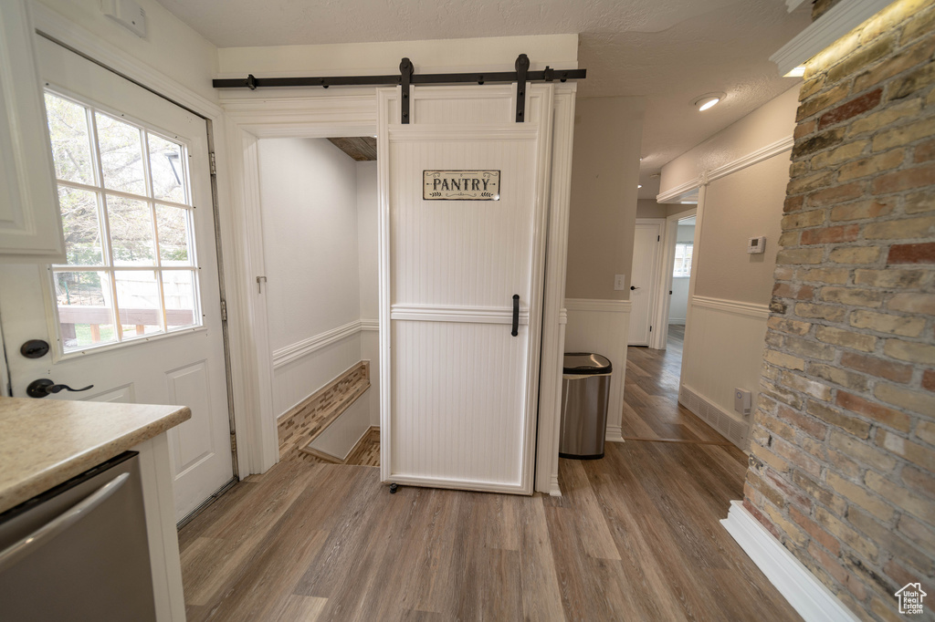 Kitchen with a barn door, dishwasher, light wood-style flooring, a wainscoted wall, and light countertops