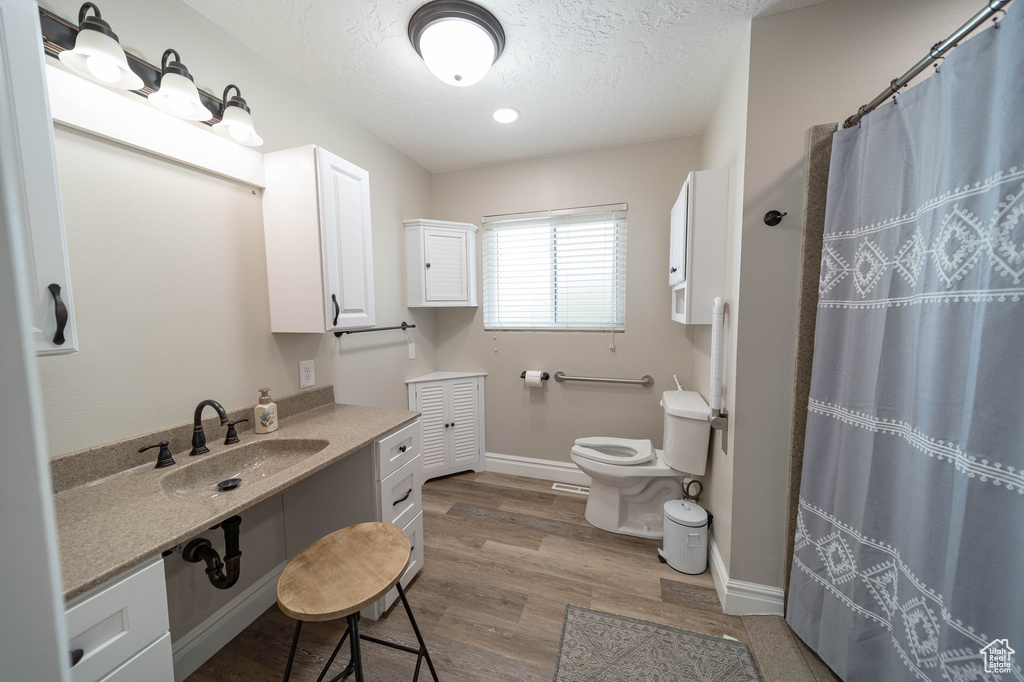 Full bath with toilet, wood finished floors, a textured ceiling, baseboards, and a shower with shower curtain