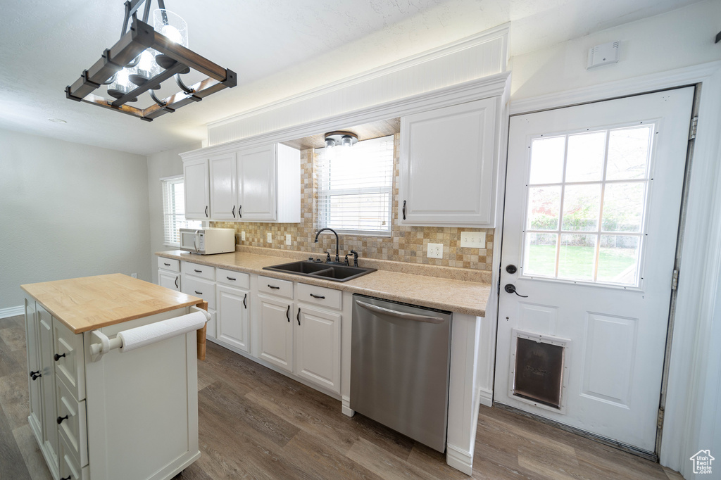 Kitchen with stainless steel dishwasher, a sink, wood finished floors, tasteful backsplash, and a chandelier