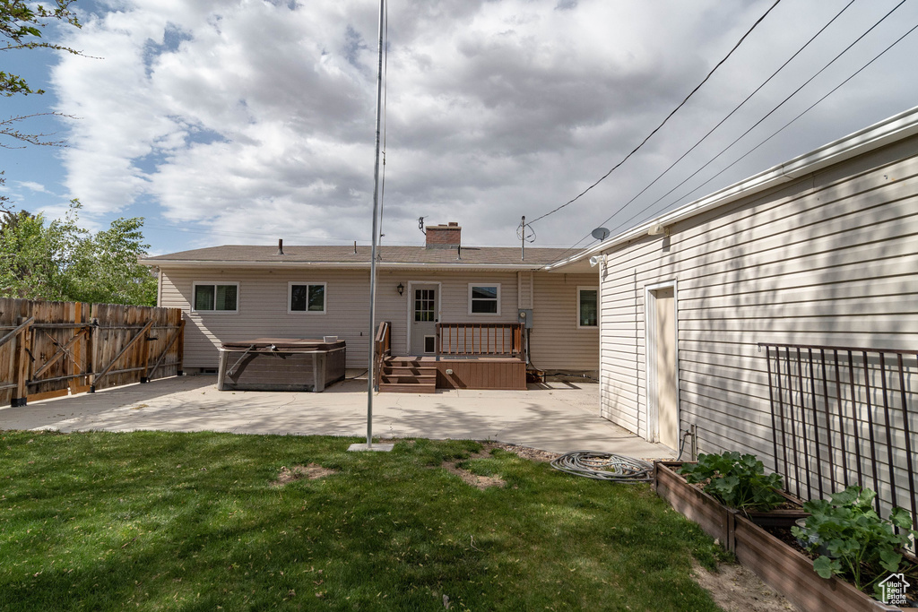Back of property featuring a hot tub, a patio, a chimney, and a wooden deck