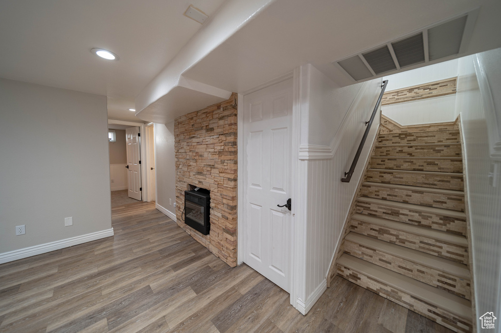 Unfurnished living room featuring wood finished floors, baseboards, a stone fireplace, stairs, and recessed lighting