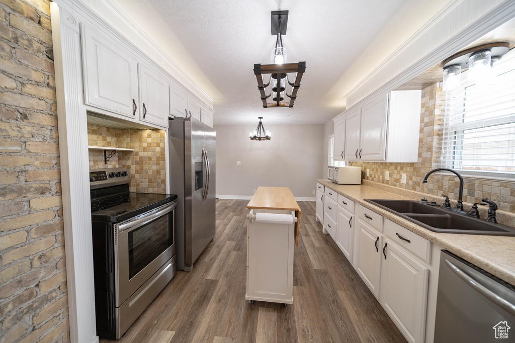 Kitchen featuring stainless steel appliances, a sink, a chandelier, white cabinetry, and backsplash