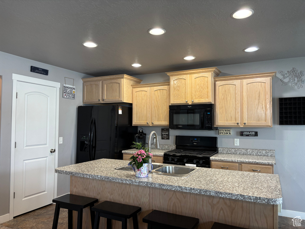 Kitchen with black appliances, light brown cabinetry, a kitchen breakfast bar, a sink, and recessed lighting