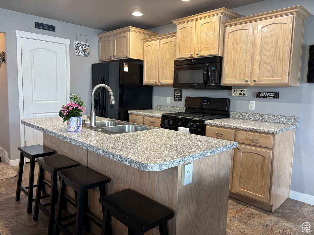 Kitchen featuring black appliances, baseboards, light brown cabinetry, light countertops, and a kitchen breakfast bar