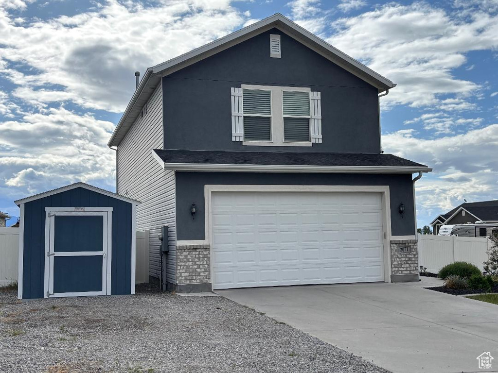 View of front of property with a storage unit, a garage, fence, concrete driveway, and an outdoor structure