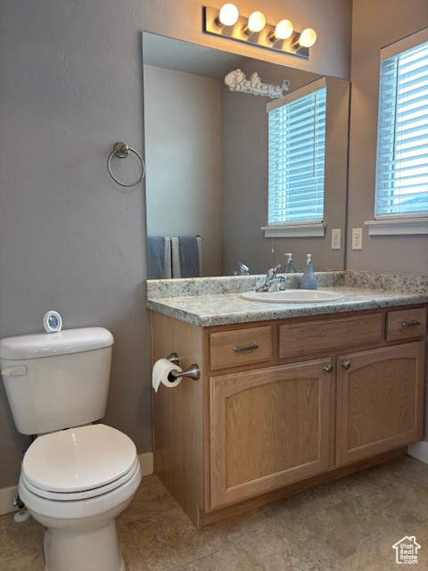 Half bathroom featuring toilet, vanity, tile patterned floors, and baseboards