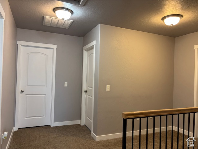Hallway with a textured ceiling, carpet, and baseboards