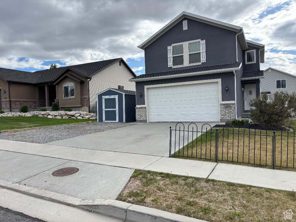 View of front of home with driveway, a storage unit, a garage, stucco siding, and stone siding