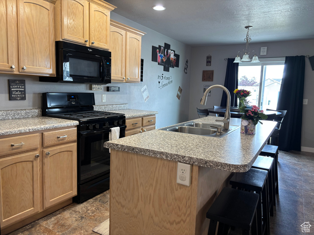 Kitchen with black appliances, a sink, light brown cabinetry, a kitchen breakfast bar, and a center island with sink