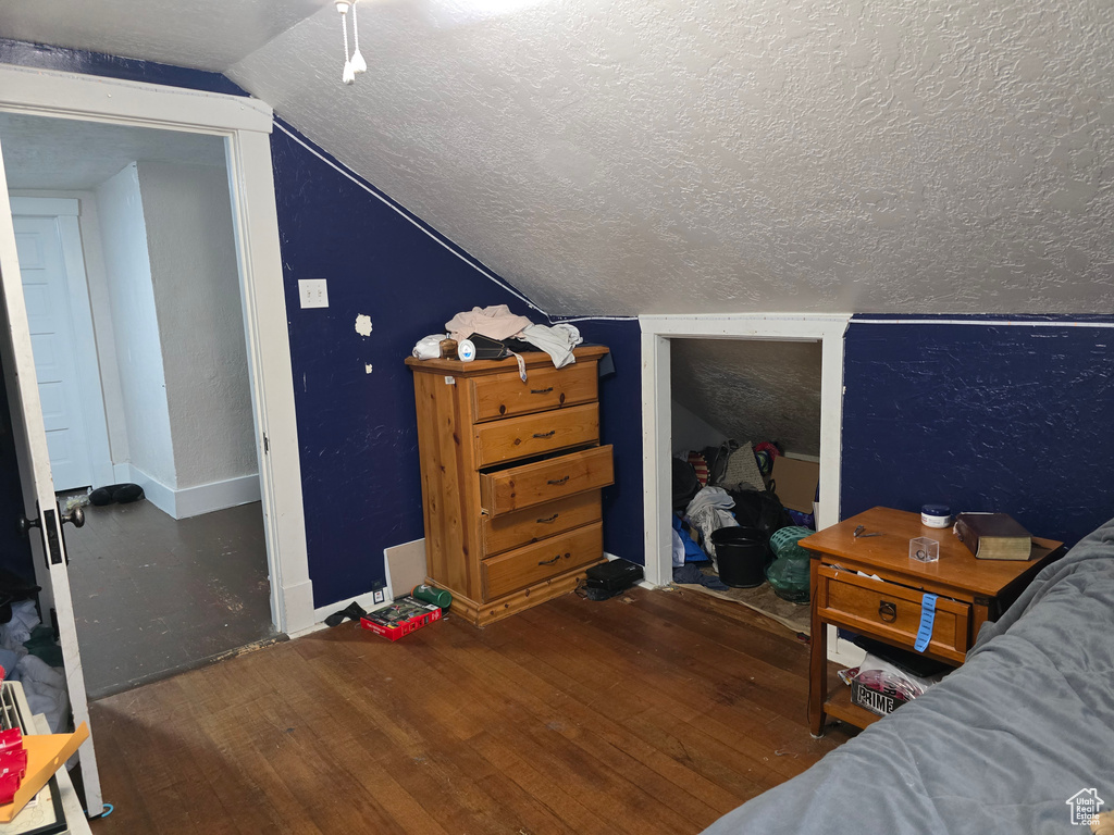 Bedroom featuring a textured ceiling, wood finished floors, vaulted ceiling, and baseboards