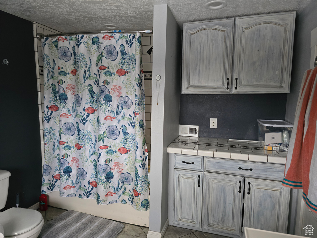 Full bath featuring toilet, a textured ceiling, shower / bath combination with curtain, baseboards, and tile patterned floors