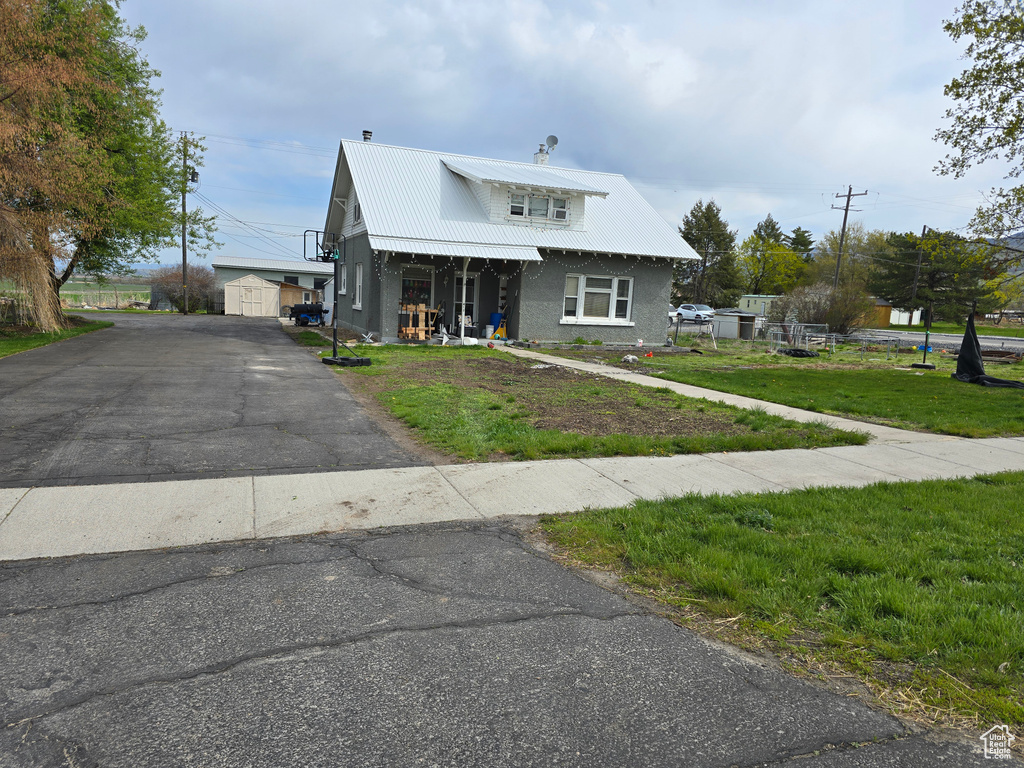 View of front facade with a front yard, an outdoor structure, a porch, metal roof, and stucco siding