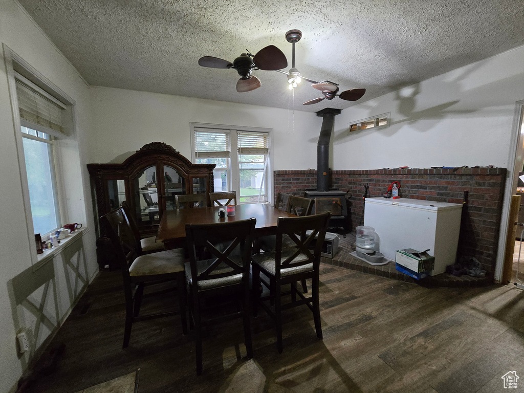 Dining space featuring a wood stove, a ceiling fan, a textured ceiling, wood finished floors, and a wainscoted wall