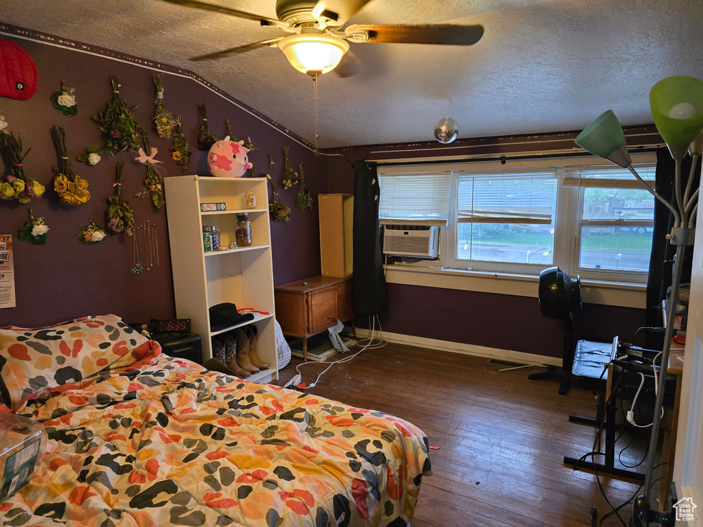 Bedroom featuring wood-type flooring, a textured ceiling, cooling unit, baseboards, and lofted ceiling