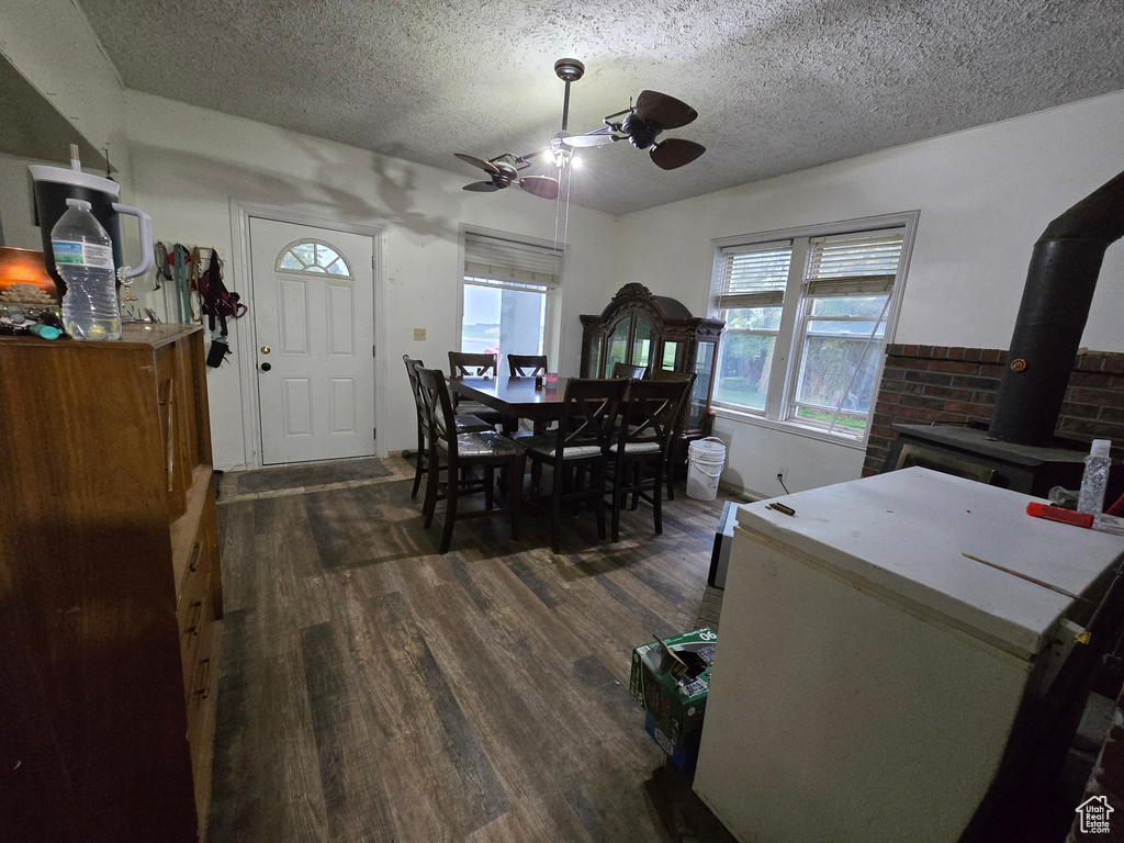 Dining space with ceiling fan, dark wood-style flooring, a textured ceiling, and a wood stove