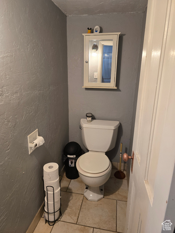 Half bathroom with toilet, tile patterned floors, and a textured wall