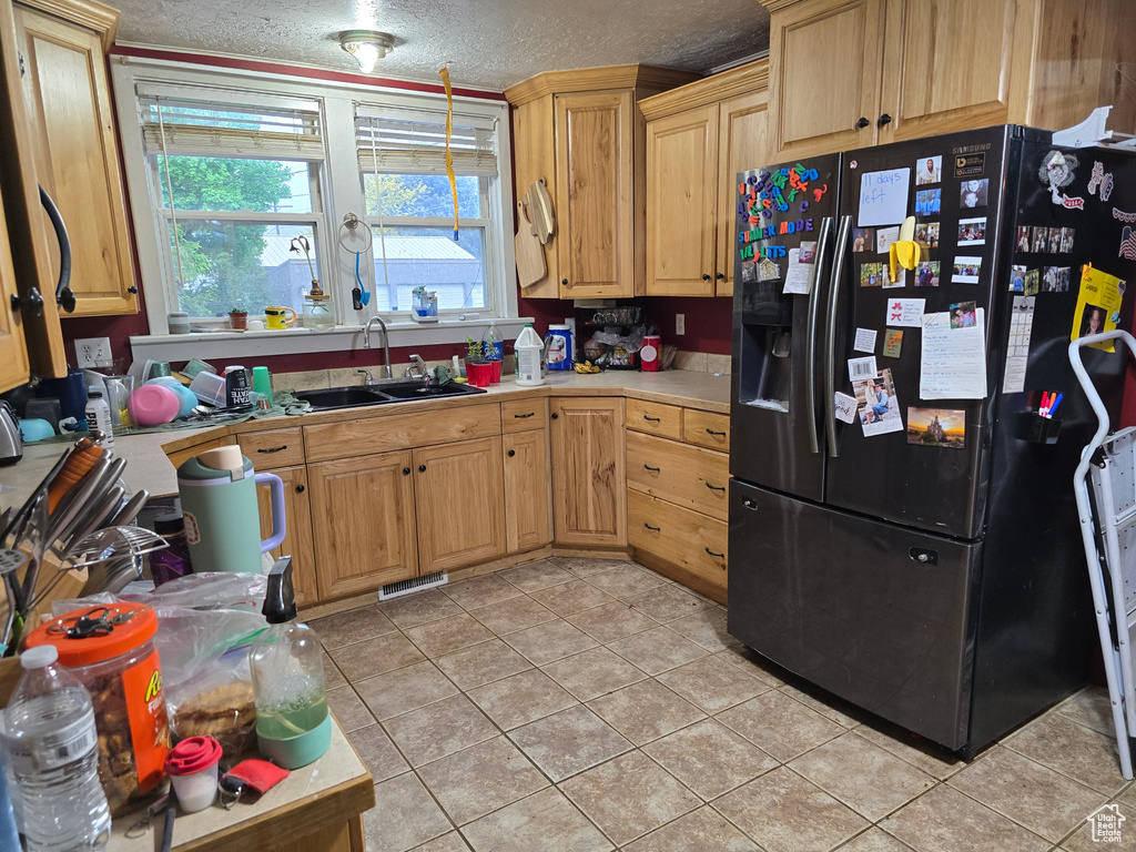 Kitchen featuring black refrigerator with ice dispenser, a sink, light countertops, light tile patterned floors, and a textured ceiling