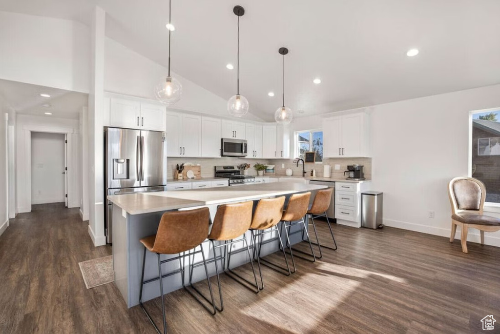Kitchen with appliances with stainless steel finishes, dark wood-style flooring, a kitchen island, white cabinetry, and light countertops