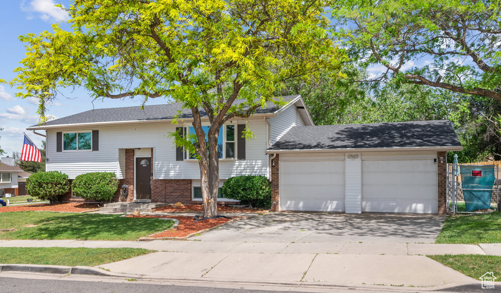 Raised ranch featuring a garage, brick siding, and driveway