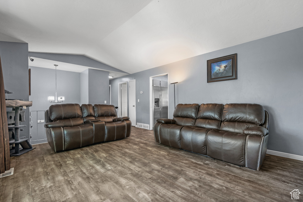 Living room featuring lofted ceiling, wood finished floors, baseboards, a wood stove, and a chandelier