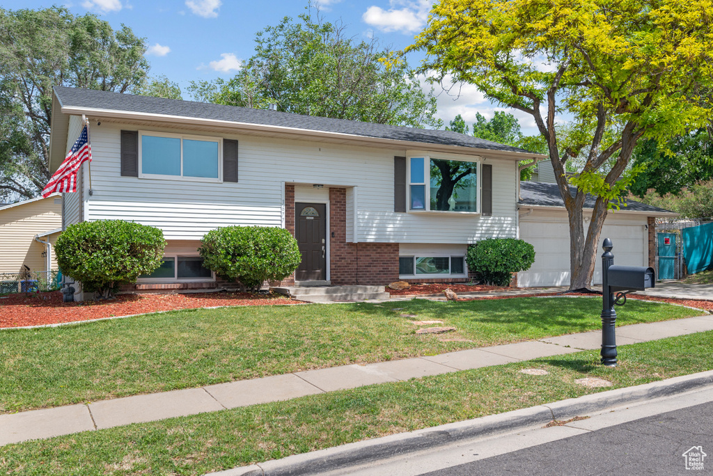Raised ranch featuring a front lawn, brick siding, and an attached garage