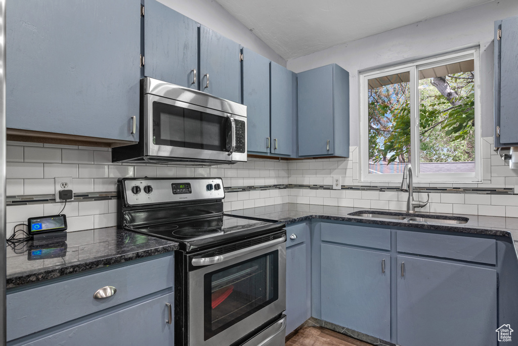 Kitchen featuring appliances with stainless steel finishes, a sink, blue cabinets, tasteful backsplash, and dark stone countertops