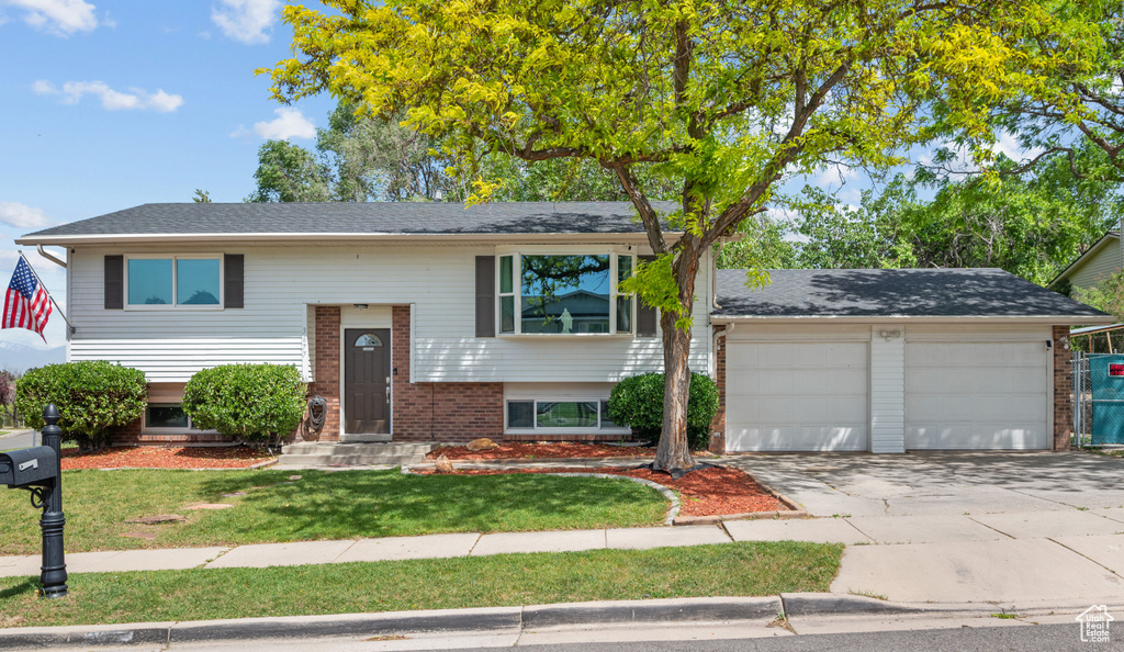 Raised ranch featuring brick siding, concrete driveway, a garage, and a front yard