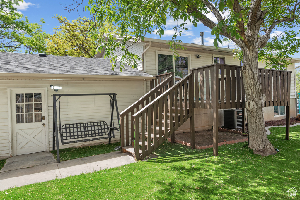 Back of property featuring central AC, a yard, a wooden deck, and a shingled roof