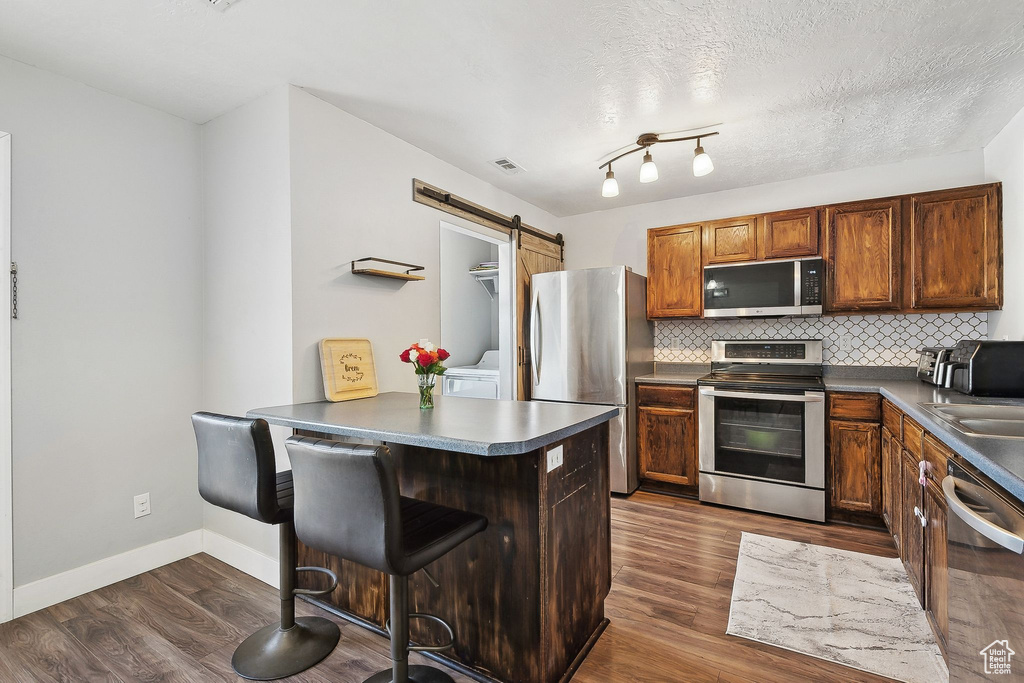 Kitchen featuring appliances with stainless steel finishes, a peninsula, dark countertops, a barn door, and decorative backsplash