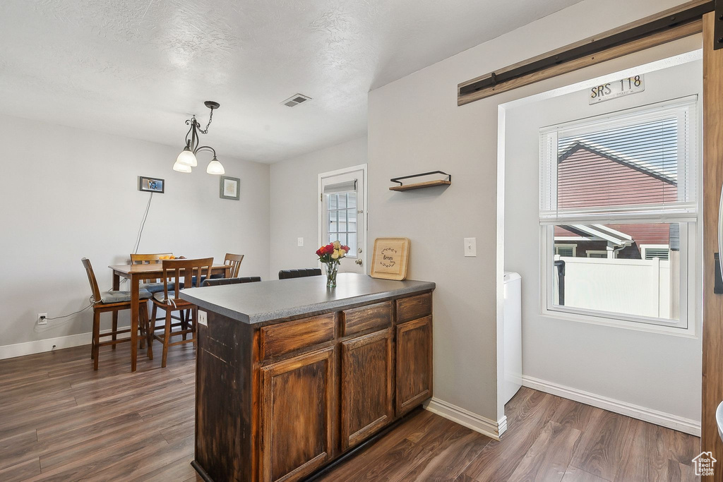 Kitchen with dark wood-style flooring, a peninsula, decorative light fixtures, and baseboards