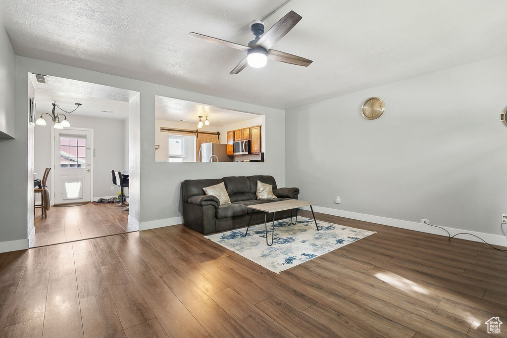 Living room with dark wood-style floors, ceiling fan, baseboards, and a chandelier