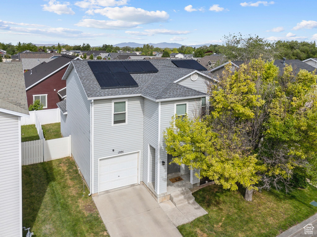 View of front facade featuring roof with shingles, a garage, solar panels, driveway, and a residential view