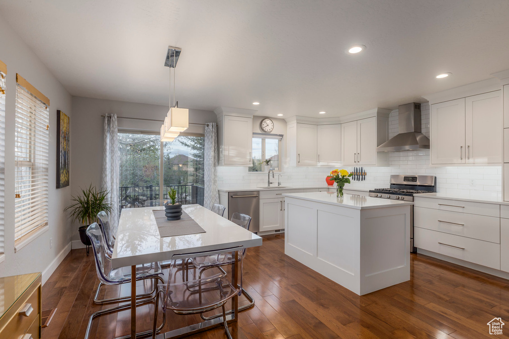 Kitchen featuring wall chimney range hood, stainless steel appliances, white cabinets, dark wood finished floors, and recessed lighting