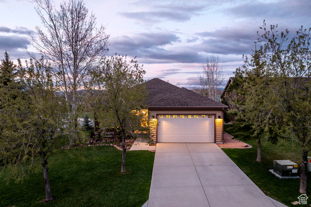 Ranch-style home featuring driveway, a lawn, an attached garage, and a shingled roof