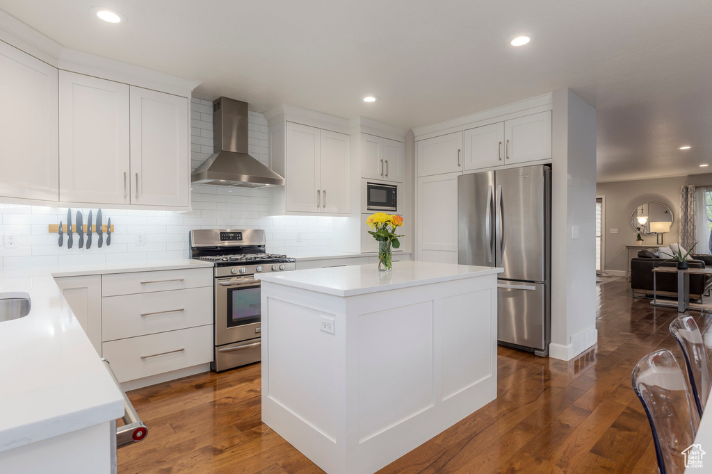Kitchen featuring wall chimney range hood, stainless steel appliances, backsplash, dark wood-type flooring, and recessed lighting