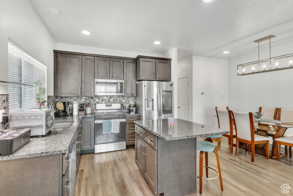 Kitchen with stainless steel appliances, light wood-style floors, a kitchen breakfast bar, decorative backsplash, and stone counters
