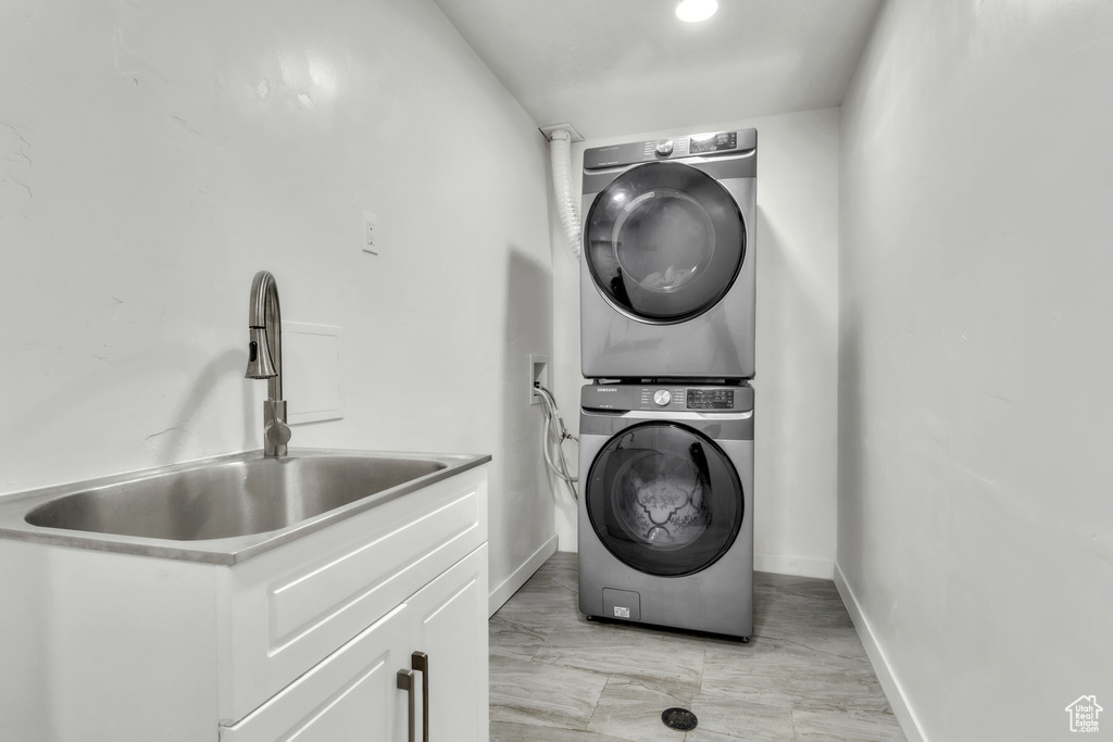 Clothes washing area featuring estacked washer and dryer, light marble finish flooring, and baseboards